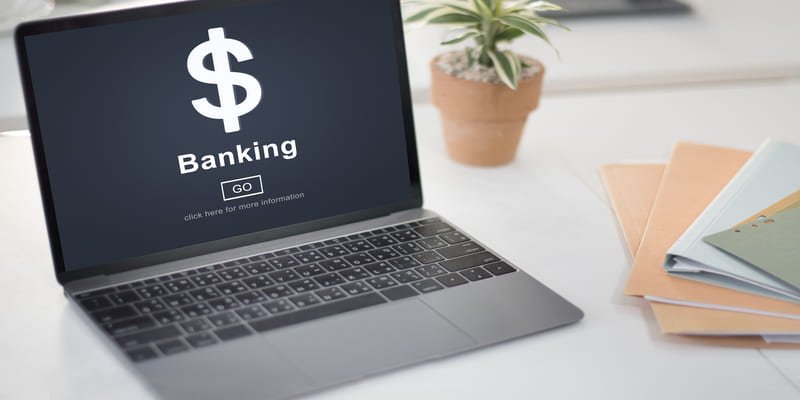 Open Banking: O Compartilhamento de Dados que Transforma o Setor 2 Um laptop com um ícone de cifrão e a palavra "Banking" na tela, representando a digitalização do setor financeiro e a transição para o Open banking.