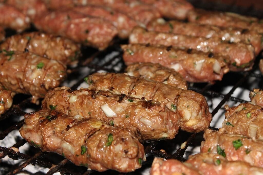 Espetinhos de carne (cevapi) artesanais sendo grelhados, com a superfície caramelizada e suculenta, prontos para serem vendidos como petisco caseiro e gerar uma nova fonte de renda extra