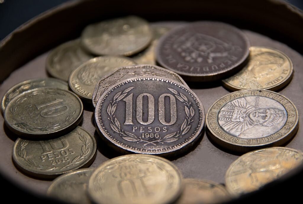Um close-up de várias moedas antigas chilenas, com destaque para uma moeda de 100 Pesos de 1986.