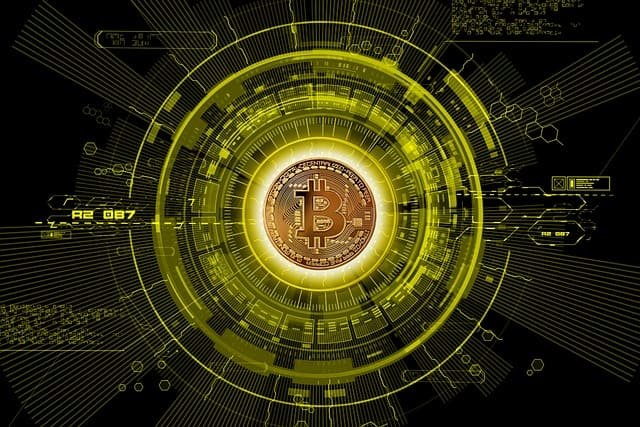 Uma representação digital e futurista de uma moeda de Bitcoin dourada e brilhante, colocada no centro de um design tecnológico radial em tons de amarelo e verde-limão vibrantes. O fundo é preto, realçando a complexa interface de dados e linhas que circundam a moeda, sugerindo a tecnologia blockchain, criptografia e o conceito de dinheiro digital. A imagem evoca temas de finanças tecnológicas e cibersegurança.
