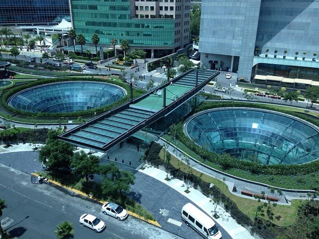 Vista aérea de um complexo de escritórios moderno, com edifícios de lajes corporativas e uma praça com duas grandes estruturas circulares de vidro. Este cenário de alto padrão imobiliário representa um ativo comercial onde os cotistas de FIIs exercem o seu poder de Voto em assembleias.